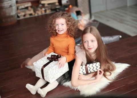 Two little sisters with gift boxes, sitting on the floor in a cozy living room. Stock Photos
