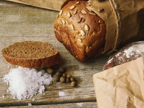 Two Loaves of Bread packed in paper on wooden table with salt and papper Stock Photos