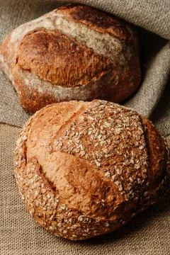Two loaves of delicious rustic bread lie on a burlap-covered surface. Stock Photos