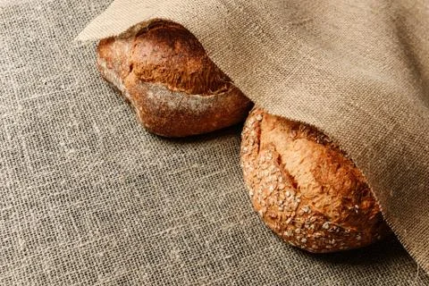 Two loaves of rustic bread lie on a burlap Stock Photos