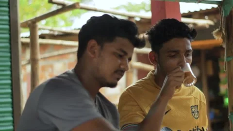 Two local young men are sitting at a tea stall, drinking tea and chatting. Stock Footage 296526200