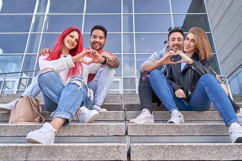 Two lovely young couples making hearts with their hands while sitting on the 스톡 사진