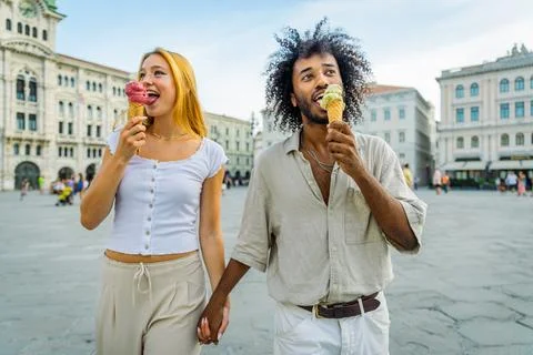 Two lovers hold hands while eating ice cream together in the city center Foto stock