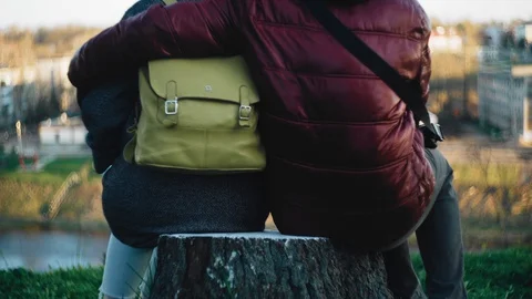 Two lovers sit on a stump on the river embankment. Rear view. A man and a woman Stock Footage 129525509