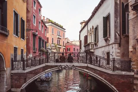 Two lovers sitting side by side on a bridge over a canal among pink buildings Stock Photos