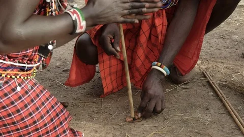 Two maasai men use a hand drill to start a fire at a manyatta in kenya Stock Footage 69812816