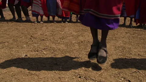 Two Maasai Perform Traditional Dance as Village Sings (with sound) Stock Footage 134843630