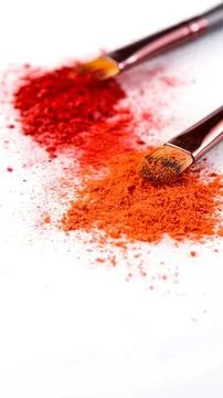 Two makeup brushes with red and orange powder on white Stock Photos