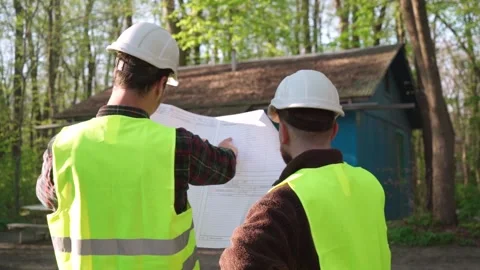Two male construction workers looking at a blueprint in front of an old house. Stock Footage 241178073