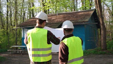 Two male construction workers looking at a blueprint in front of an old house. Stock Footage 242166649