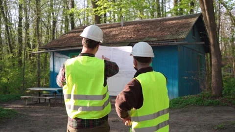 Two male construction workers looking at a blueprint in front of an old house. Stock Footage 243293231