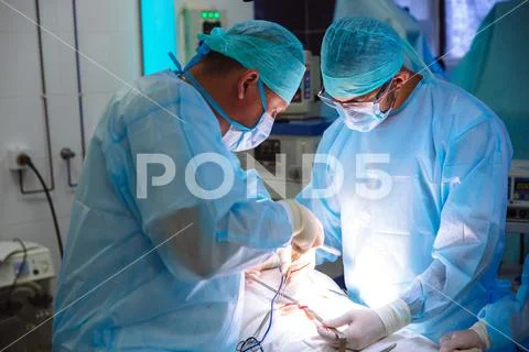 Two male doctors in sterile medical clothes perform an operation in a hospital Stock Photos