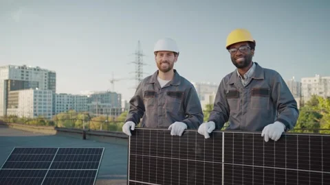 Two male engineers standing on a rooftop holding a solar panel, smiling in work Stock Footage 300886447