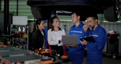 Two male EV technicians discuss laptop diagnostics with two Asian female Stock Footage 345959961