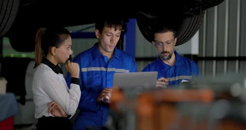 Two male EV technicians examine laptop data beside Asian female customer under Stock Footage 345959852