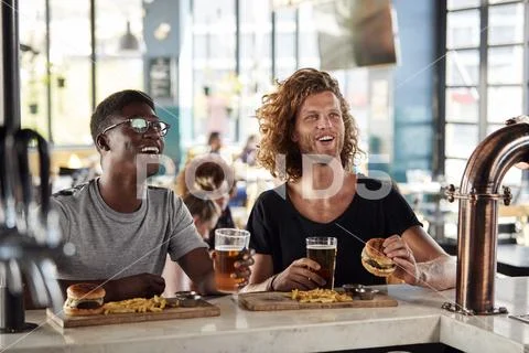 Two Male Friends Eating Food And Drinking Beer In Sports Bar Stock Photos