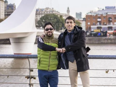 Two male friends hugging while looking at camera near Puente de la Mujer (W.. Stock Photos