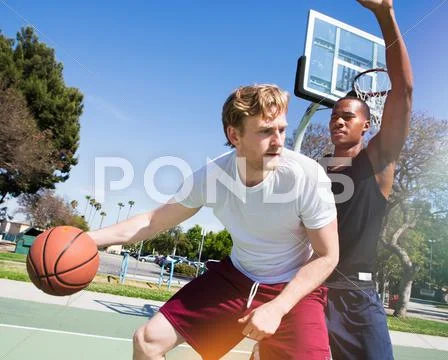 Two Male Friends Playing Basketball On Outdoor Court