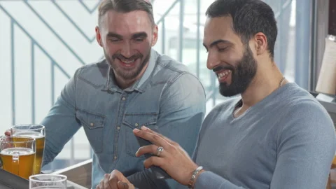 Two male friends using smart phone while drinking beer together Stock Footage 148764485