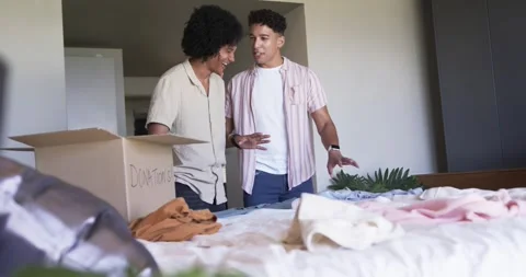 Two male partners pointing at clothes, sorting, folding, packing DONATIONS box Stock Footage 336784728