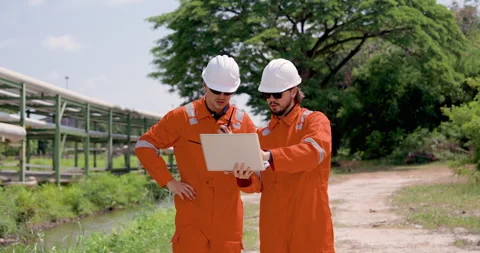 Two male refinery engineer review laptop data beside pipeline route, planning Stock Footage 337391359