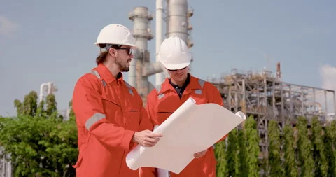 Two male refinery engineer study blueprint near processing unit, reviewing Stock Footage 334834079