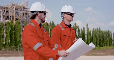 Two male refinery worker carry blueprint beside plant unit, walking through site Видео 344392448