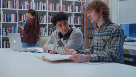 Two male students studying together in a library 스톡 동영상 335125064