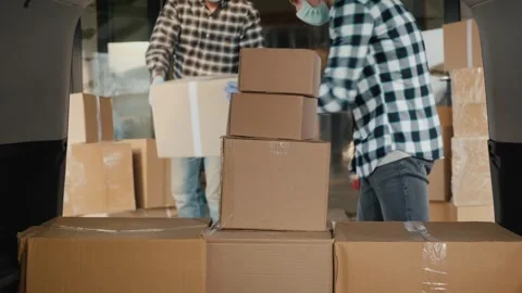 Two male warehouse workers wearing masks and gloves loading cardboard boxes.. Stock Footage 334550960