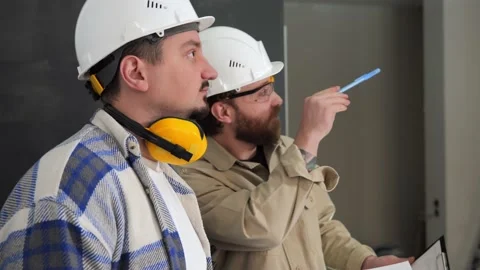 Two male workers are considering a repair plan while standing indoors Stock Footage 235169190