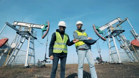 Two male workers are talking in front of functioning oil-derricks. Energy, oil Video stock 98169818