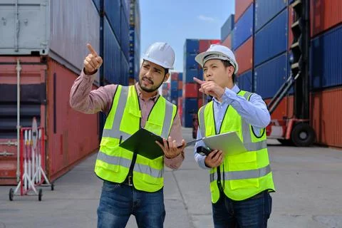 Two male workers work at a logistics terminal with many stacks of containers. Stock Photos