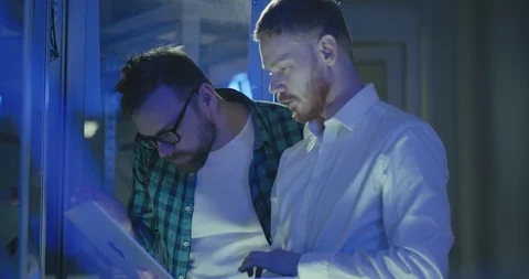 Two male young IT system administrators discuss work using laptop in rack server Stock Footage 107902800