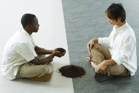 Two males sitting face to face, one holding out handful of soil Stock Photos