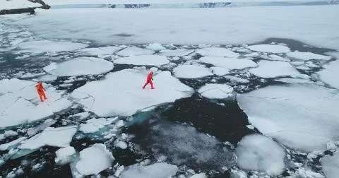 Two man in immersion suits run melting arctic ice Foto stock