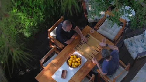 Two man playing backgammon on patio under trees. 4K Stock Footage 195647650
