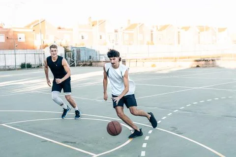 Two man running while playing basketball in an outdoor court Stock Photos