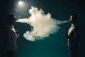 The two man smoke an electrical cigarette on the background of bright light Photo