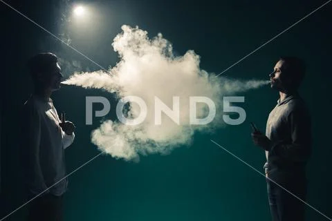 The two man smoke an electrical cigarette on the background of bright light Stock Photos