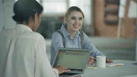 Two manager women are sitting at a table with a laptop, working and chatting Stock Footage 124328343