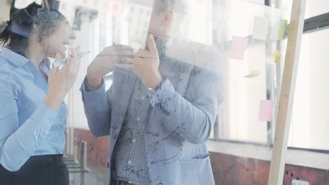 Two managers, a man and a woman, write formulas on a glass board with a marker Stock Footage 108984702