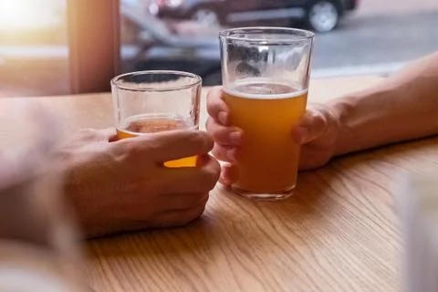 Two man's hands holding beer glasses or clinking in the pub Stock Photos