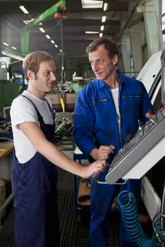 Two manual workers talking and working in a metal parts factory Stock Photos