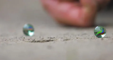 Two marbles on the ground and a third comes and falls into the hole Stock Footage 154252017