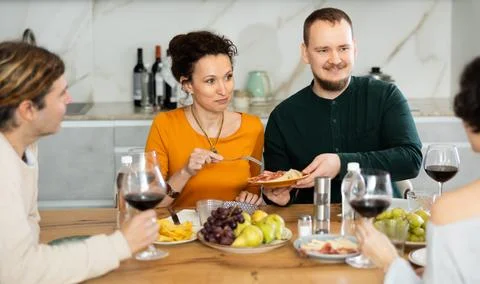Two married couples are sitting at table, enjoying food and wine, chatting Stock Photos