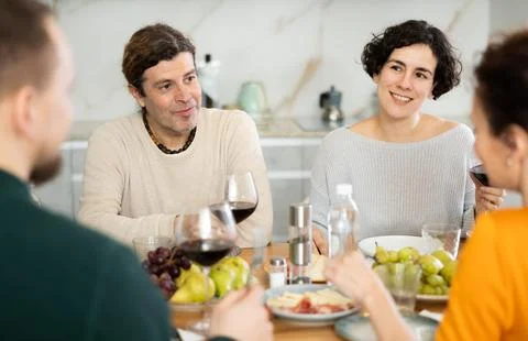 Two married couples are sitting at table, enjoying food and wine, chatting Stock Photos