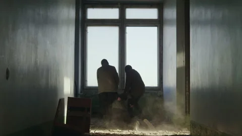 Two masked men drag a hostage across the dusty floor of an abandoned building. Stock Footage 227925740