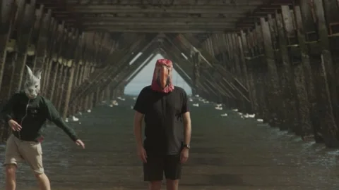 Two masked people dance under the legs of a pier. Abstract and unsettling. Stock Footage 139603883