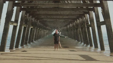 Two masked people dance under the legs of a pier. Abstract. Stock Footage 139603889