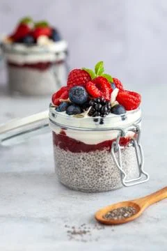 Two mason jars with chia pudding and fresh berry fruits and mint on a white b 写真素材